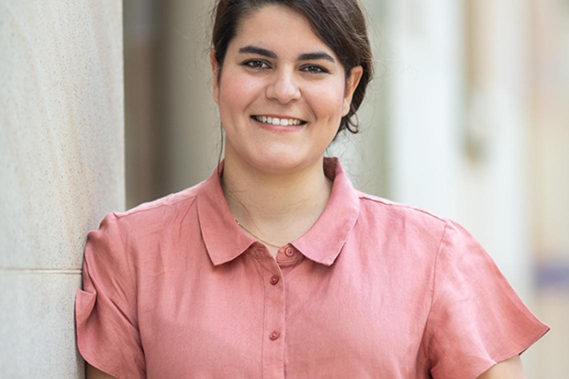 A woman leaning against a wall wearing a pale pink shirt 