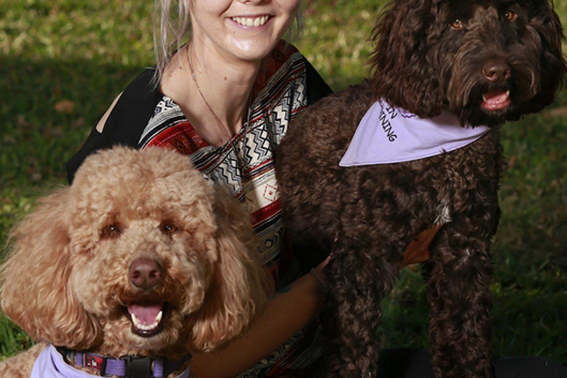 Jess sitting on the grass with two dogs each wearing a scarf