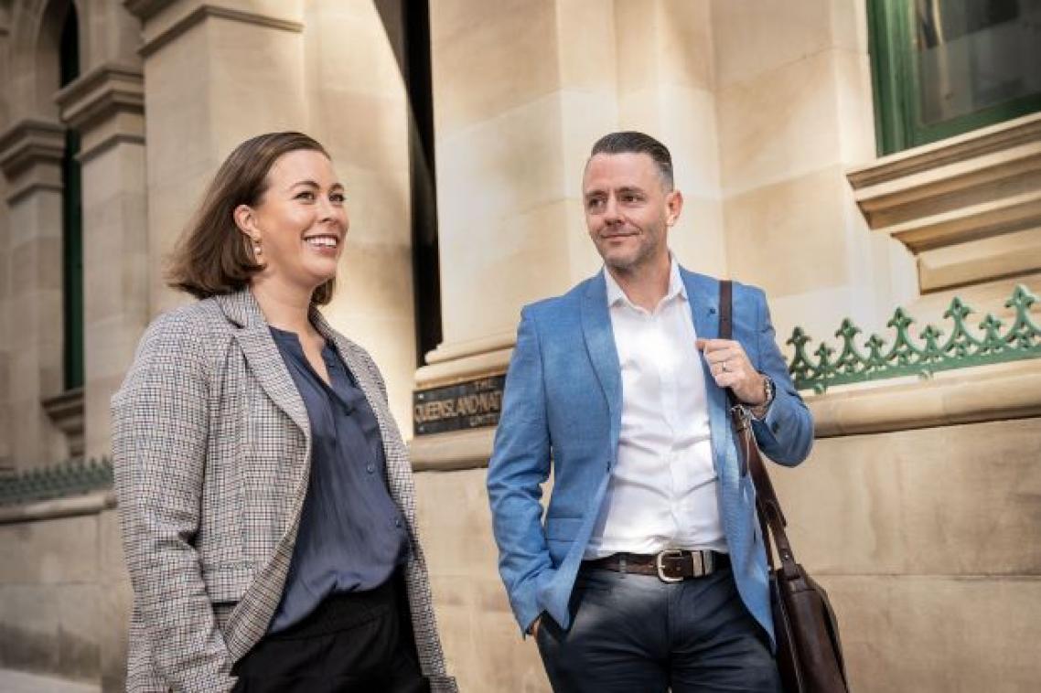 A woman and a man in business wear walking past a sandstone building