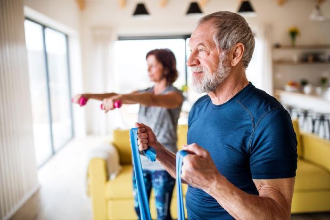 Older man and woman exercising at home with elastics and weights.