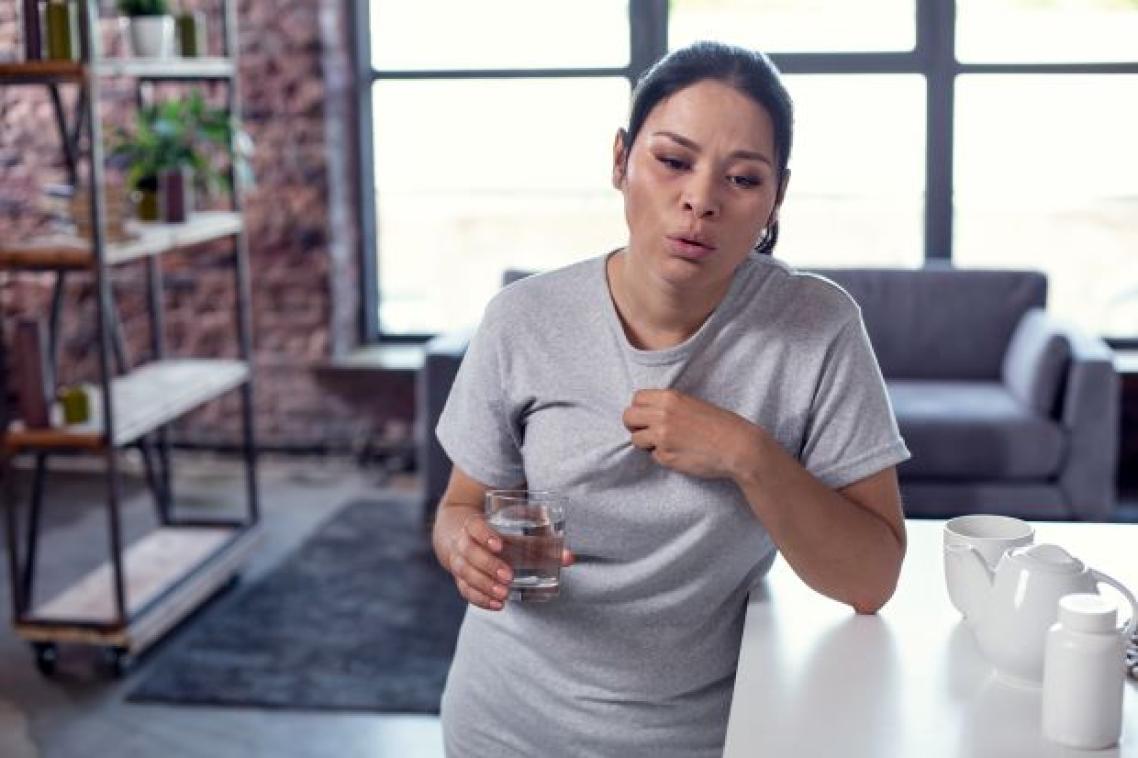 Woman leaning on bench holding glass of water looking hot and distressed. Adobe.