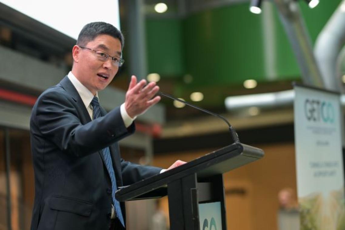 A man stands at a lectern with his hand raised.