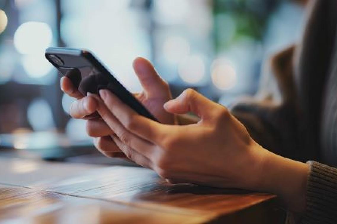 Two hands lean on a desktop holding a phone