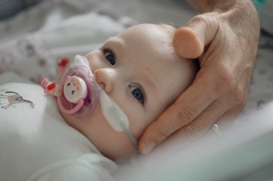 Toddler with nasal oxygen prongs insitu lying with head on pillow and sucking on dummy. Adult hand supporting head.