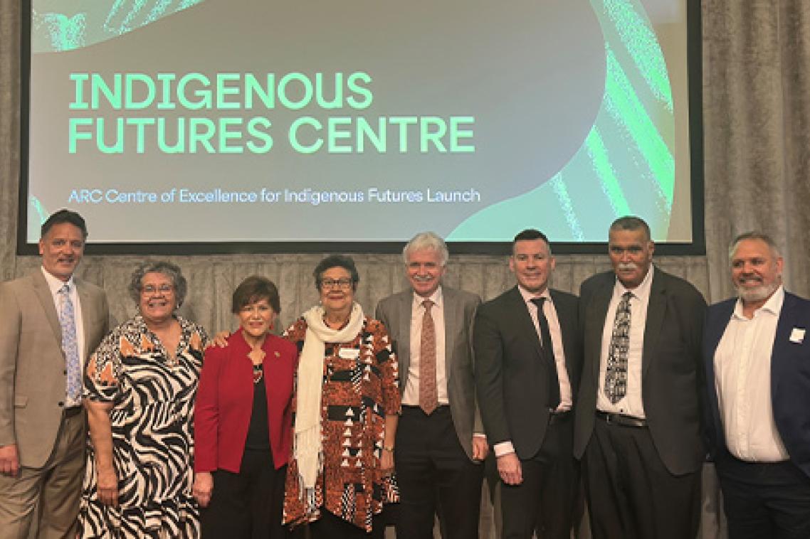 A group of men and women stand side by side on stage with a slide behind them reading Indigenous Futures Centre.