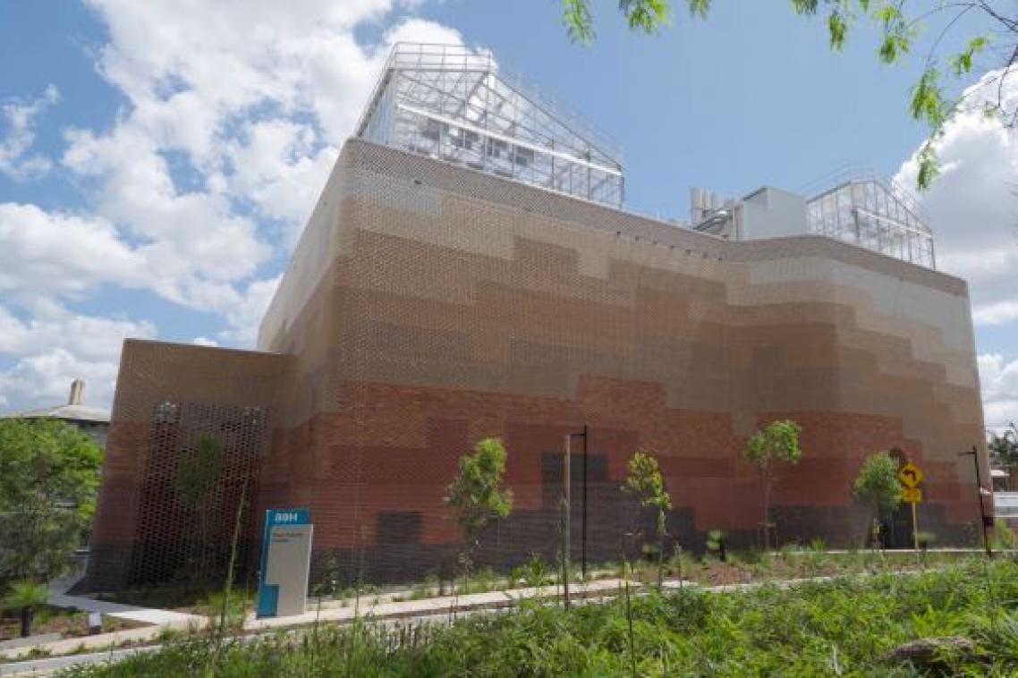 a large brick building against a blue sky with glasshouses on its roof