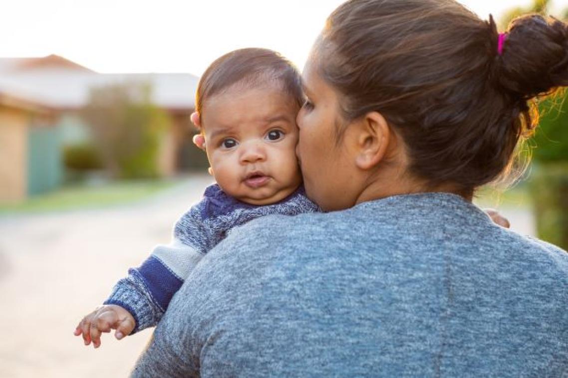 An Indigenous woman kisses a baby looking over her shoulder.