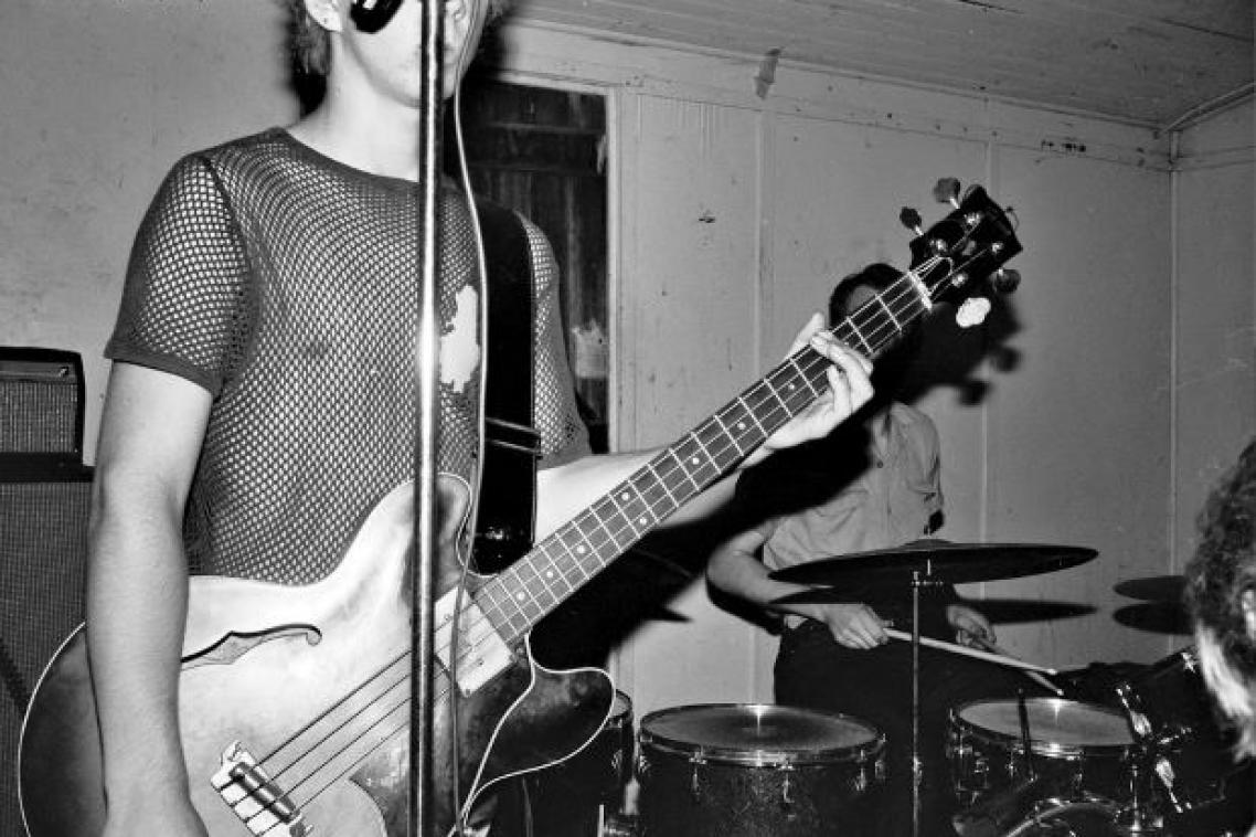 A black and white image of a male guitarist in a mesh shirt.