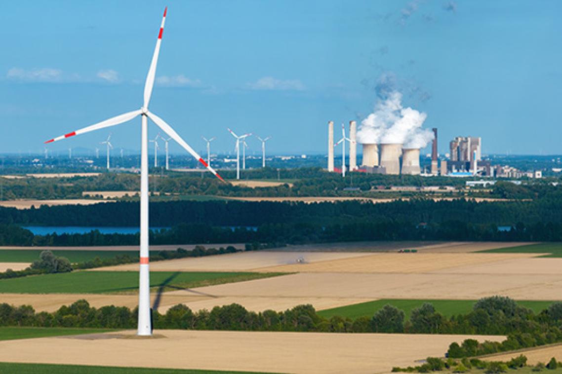 A wind turbine in a dry field with a power plant emitting steam in the background