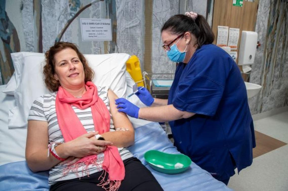 A woman lies in a hospital bed as a nurse prepares to give her a vaccine by needle. 