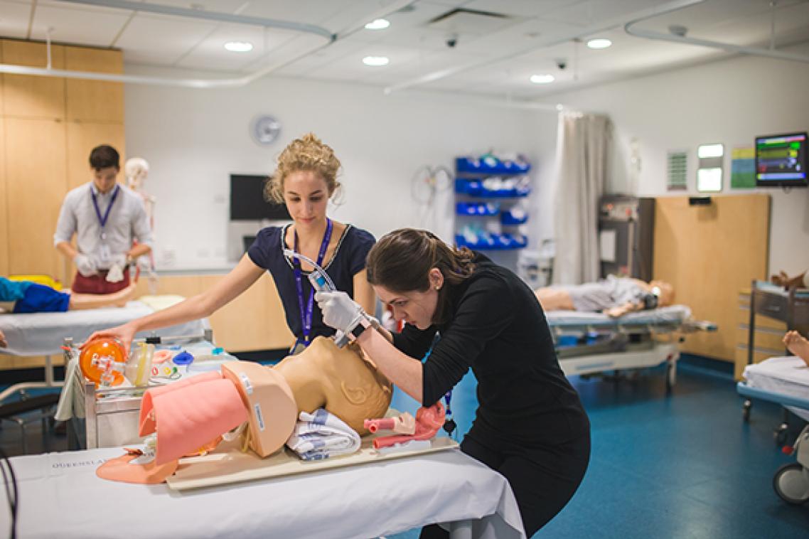 Med students practicing intubating with a dummy on a stretcher. She is bent over the head, while another woman watches