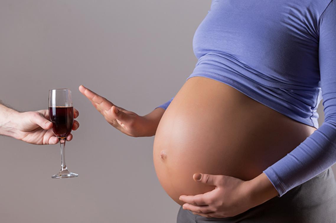 A pregnant woman waves off a glass of red wine.