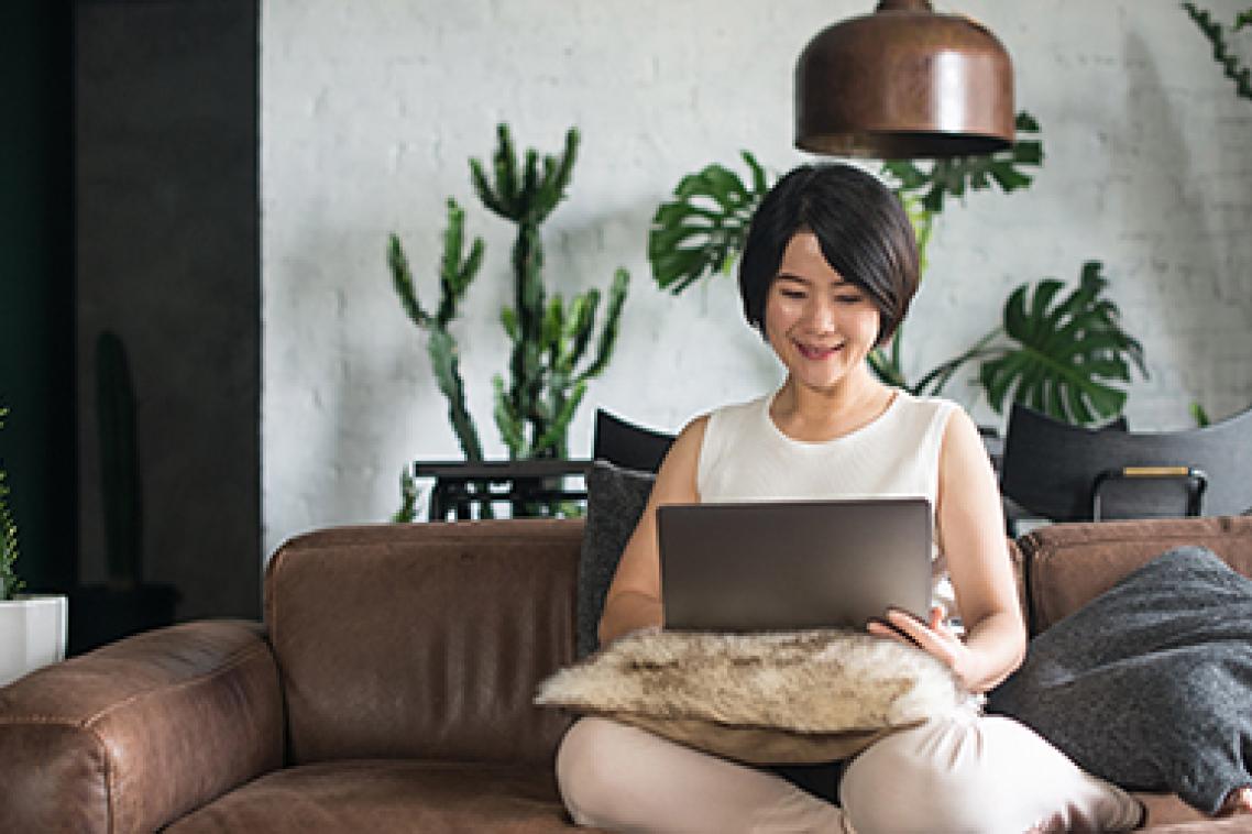 A smiling woman sitting on a couch using a laptop