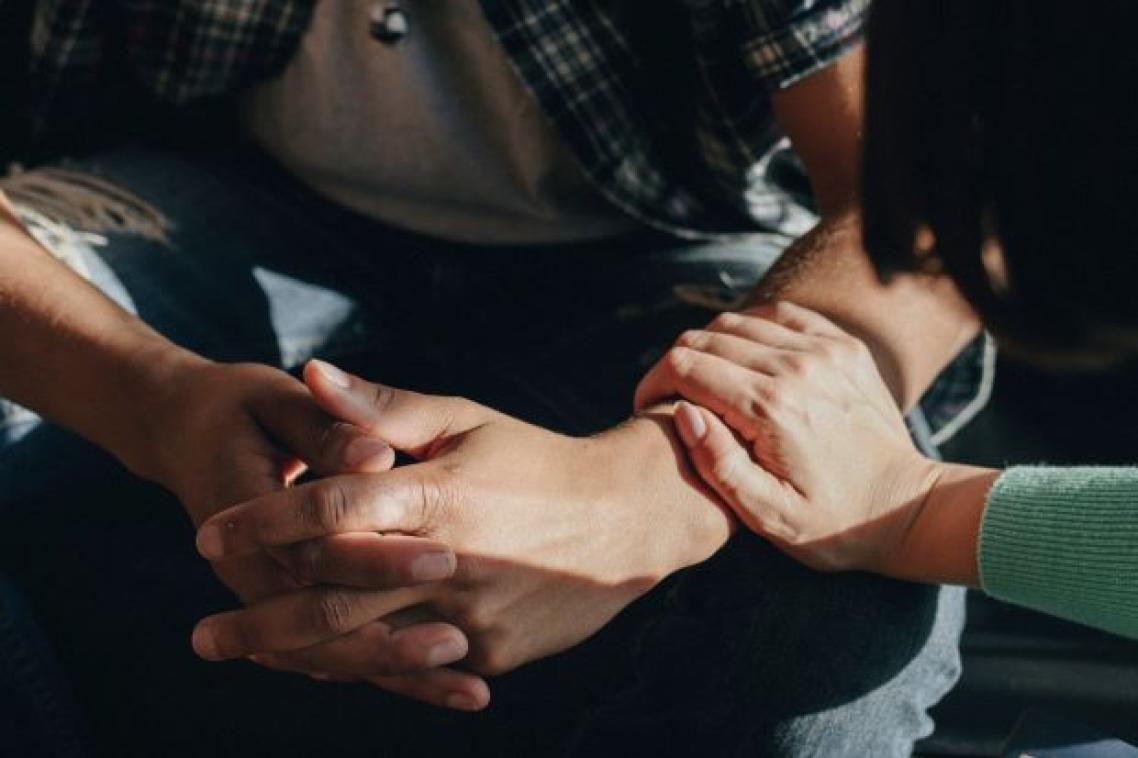 Close up of man's clenched hands with a woman's hand resting on his arm. Adobe