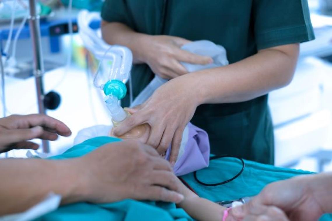 A small child is held by medical staff with a mask with tubes over their nose and mouth