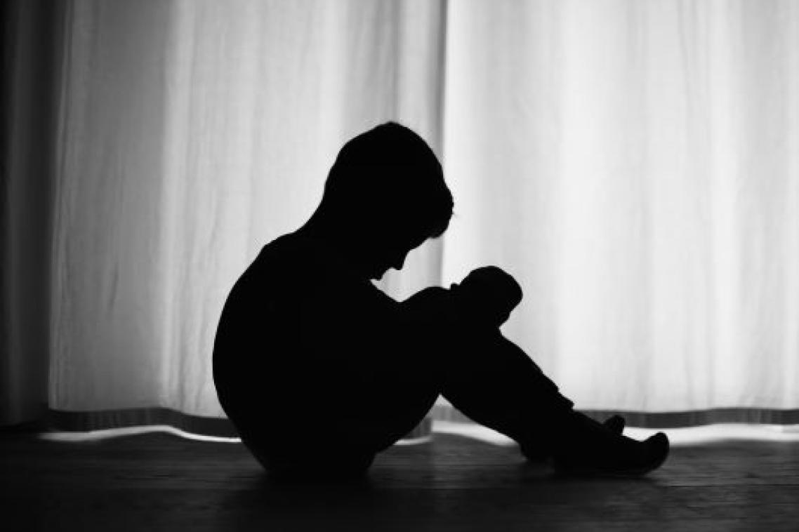 A profile photo in shadow of a young boy seated and looking down dejectedly.
