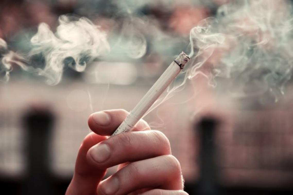 A closeup photo of fingers holding a lit cigarette with smoke wafting in the background.