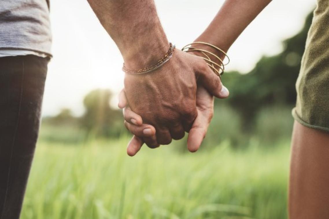A couple holding hands while walking on the grass.