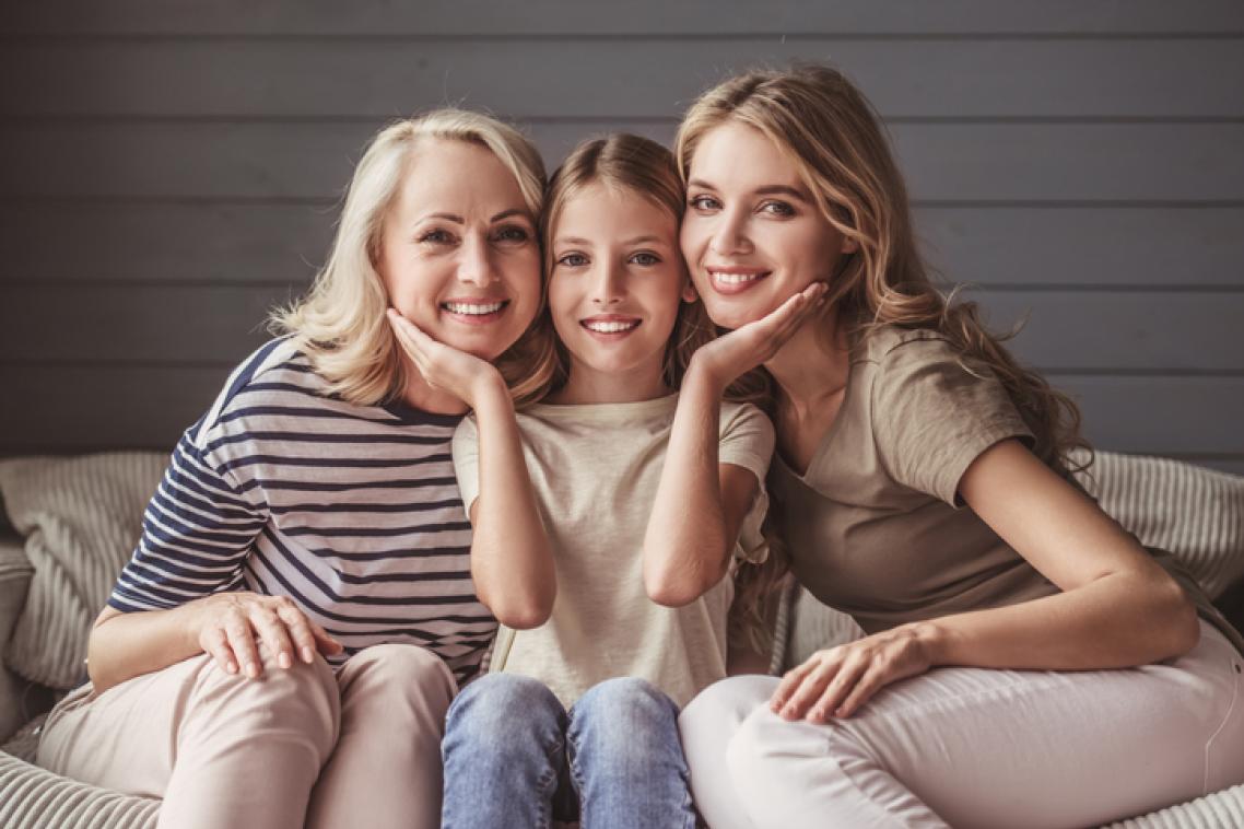 Three generations of women sit on a couch.