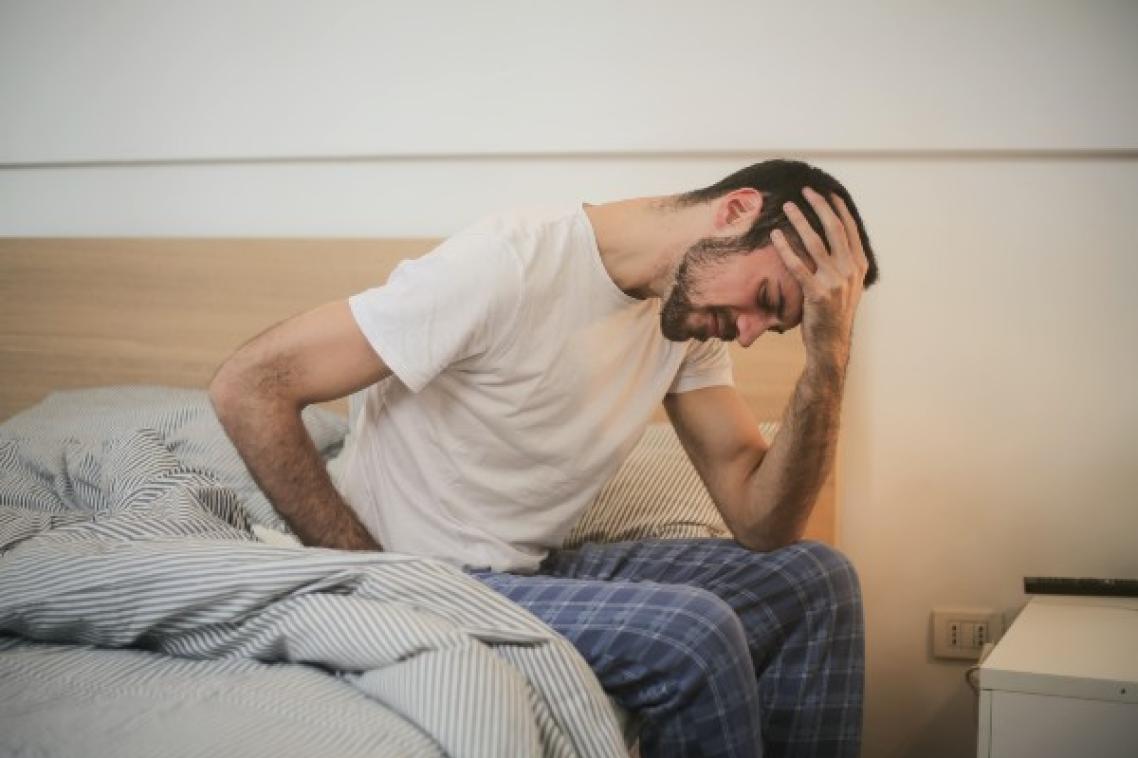Man sitting on side of bed with head in his hands.
