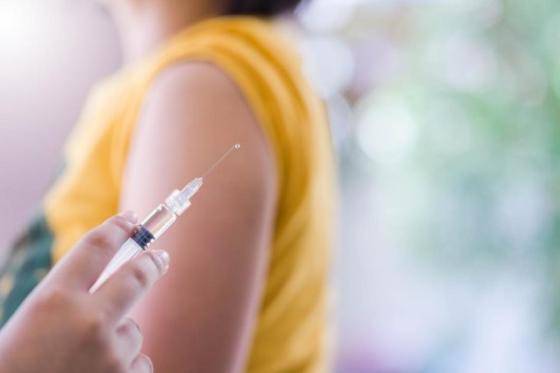 Close-up of vaccine with women in background with yellow shirt sleeves rolled up.