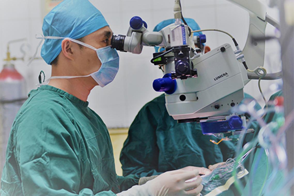 Surgeon wearing scrubs looking into eye machine