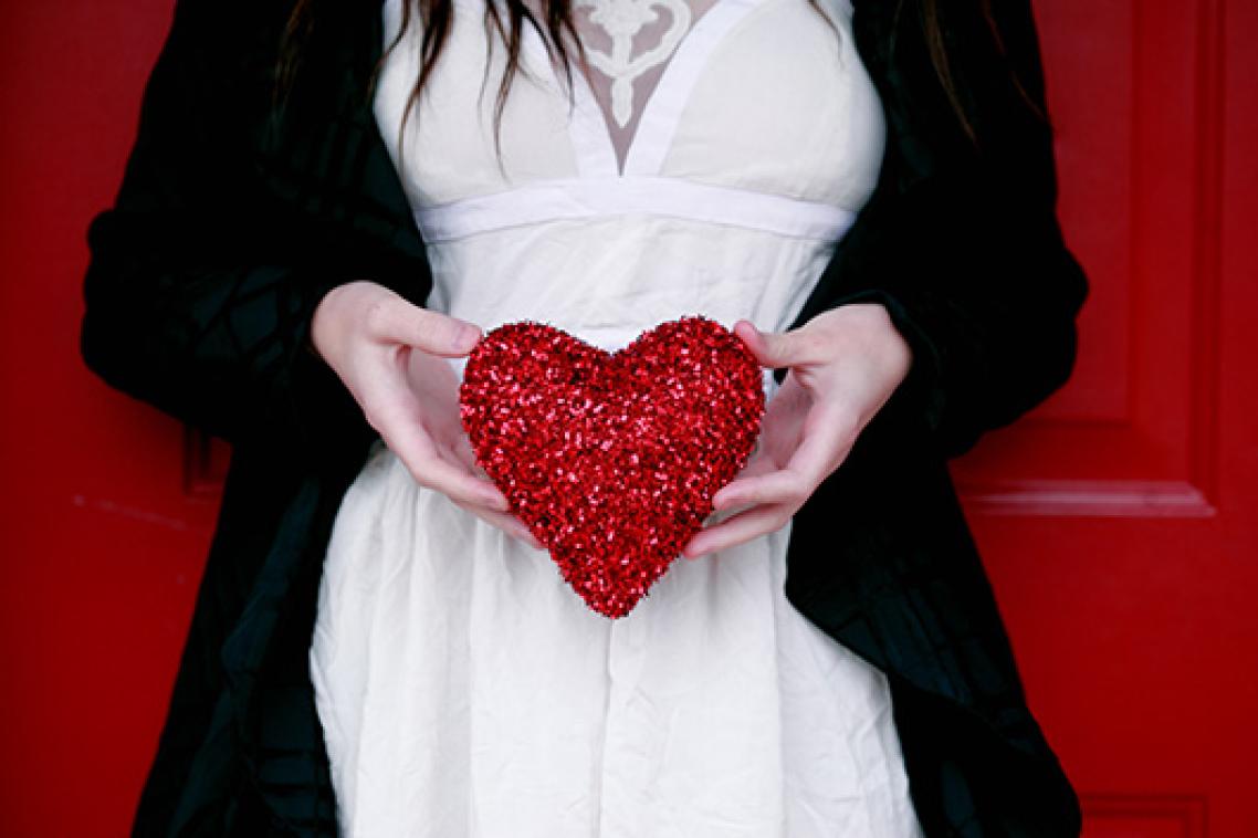 Woman holding a red heart over her stomach.