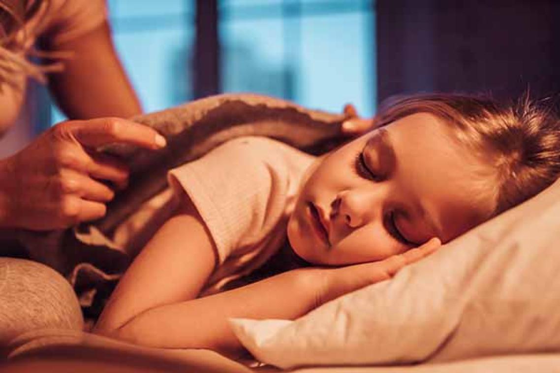 Child sleeping on her side with a mother's hands tucking the blanket around her shoulders