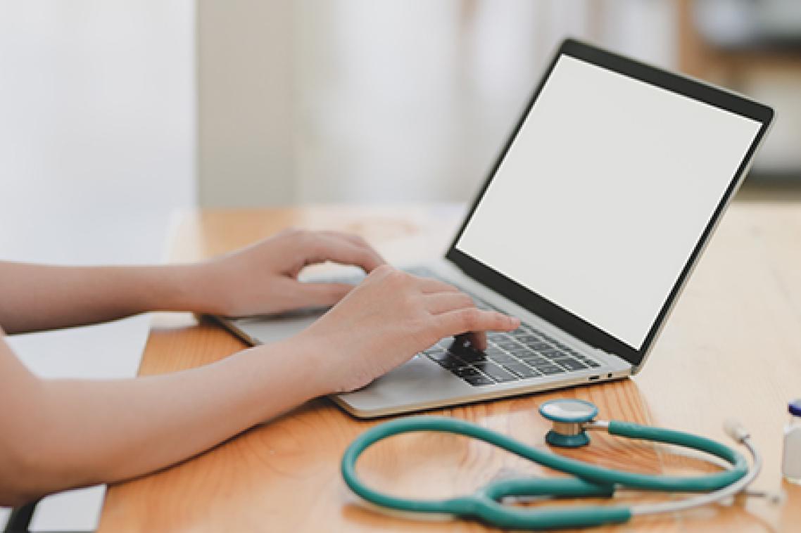 doctor typing on a laptop with a stethoscope curled about beside the keyboard, and a patient skyping or zooming for a telehealth consult 