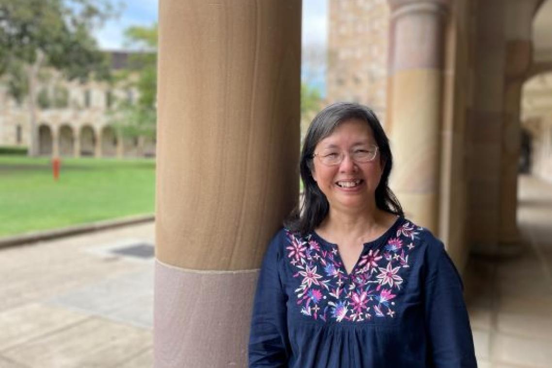 Dr Poh Hillock standing outside a sandstone building with trees behind her.
