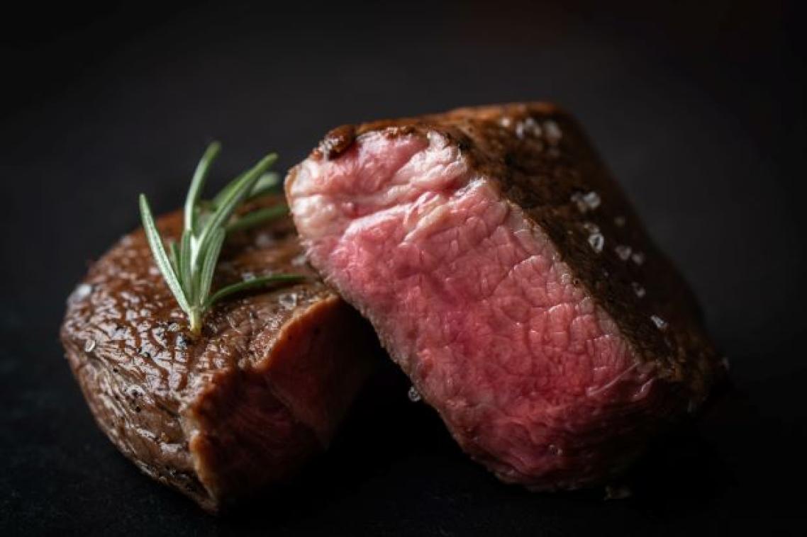 A close up image of two thick beef steaks, cooked with pink insides and some rosemary on a plate.