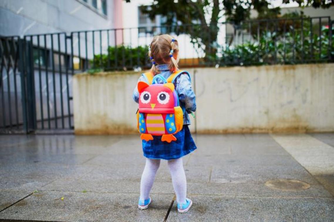 small girl with colourful backpack looks at the entrance to a daycare centre