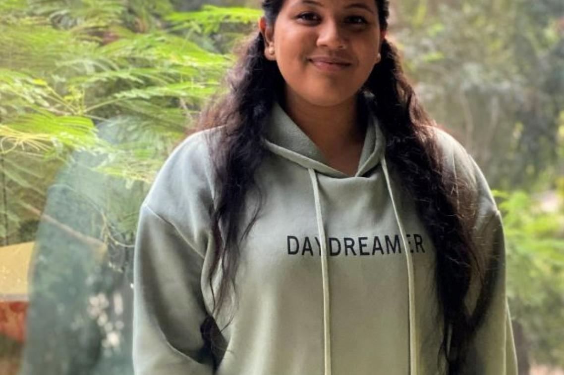 Physiotherapy student, Shali Thevarasan standing in front of a window overlooking trees. Supplied.