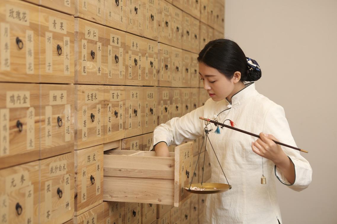 Woman looking through a drawer of Chinese medicine in a wall full of drawers