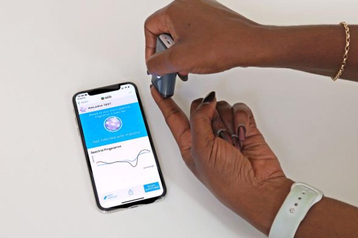 mobile phone screen next to two hands, one holding a small grey box against the fingers of the other hand