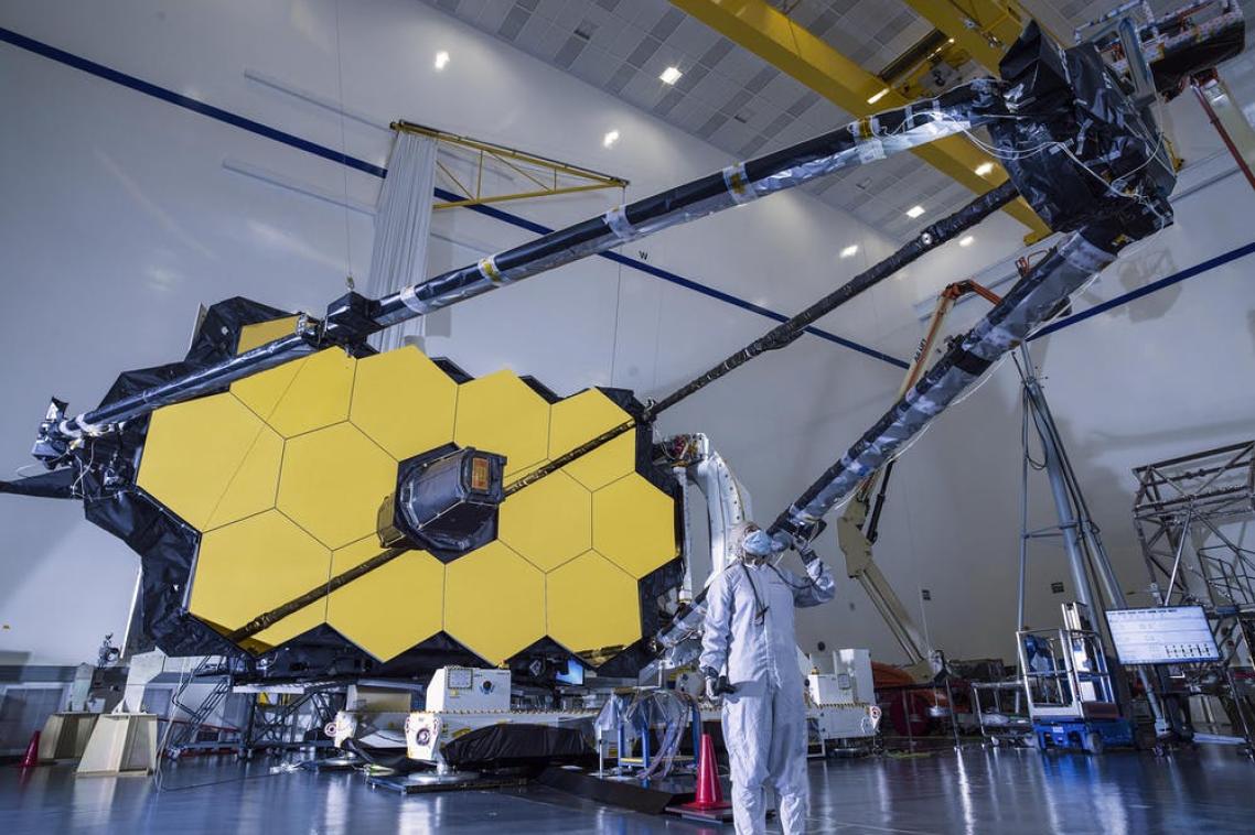 A person in a hazmat suit standing beneath a large telescope.