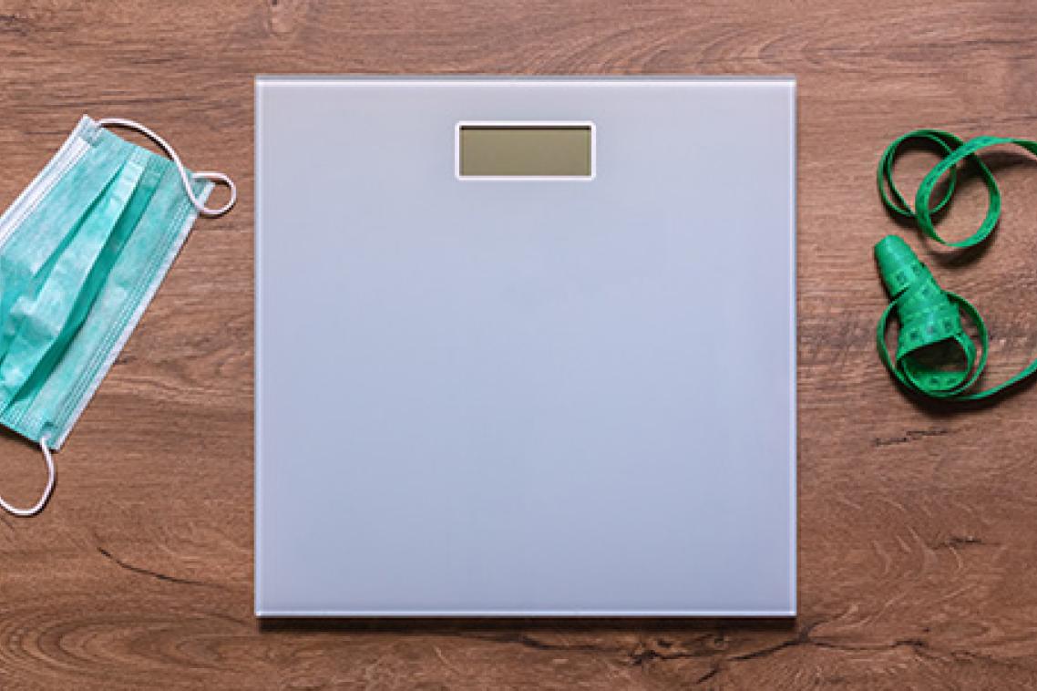 A weighing scale on a wooden floor next to a tape measure and a surgical face mask