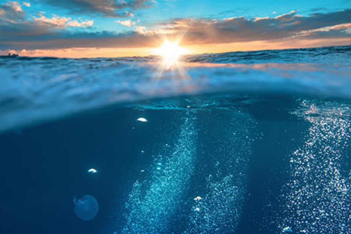 View of the ocean and sky, with the sun beaming in the centre of screen and emitting rays of golden light