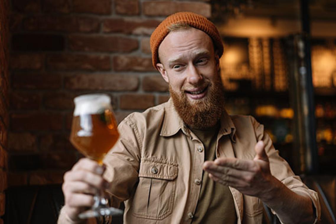 Man holding glass of beer at a distance, smiling at it. Adobe stock