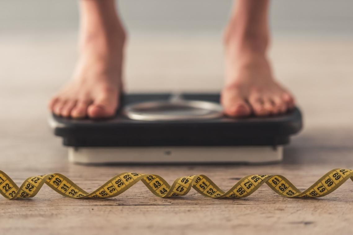Man with feet on scale with tape measure in front.
