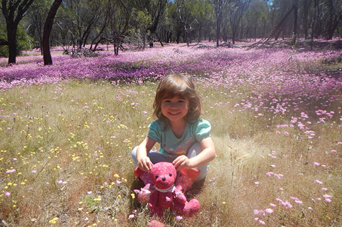 Grace Fulton sits with a stuffed toy in a field of colourful flowers