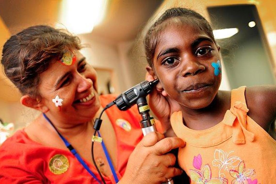 A health practitioner checks the ear of a young Indigenous girl.