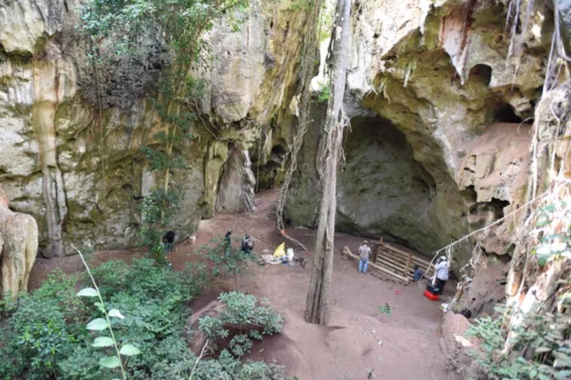 The cave in the forest in Kenya with the excavation team working at the mouth