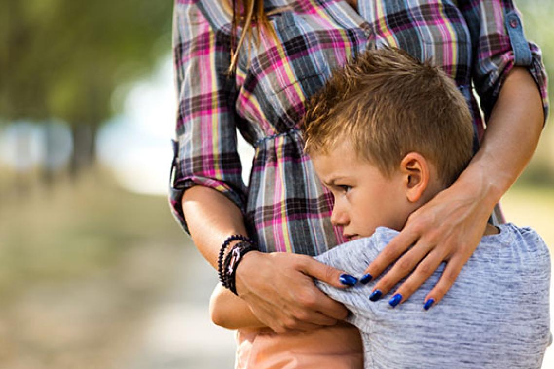 A small boy clings to his carer