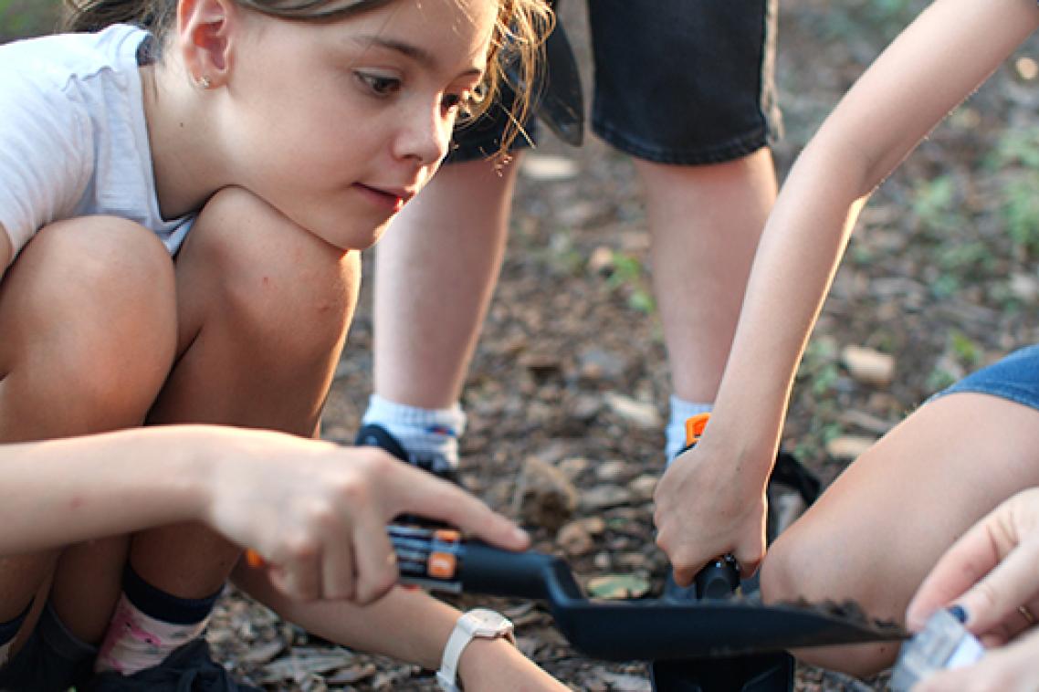 A young girl digs in the dirt to fill a Soils for Science sample bag.