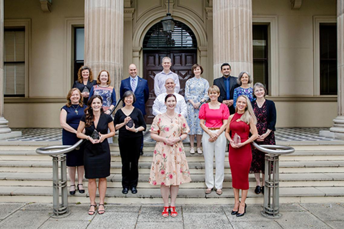 A group of people standing on the steps of a building holding awards.