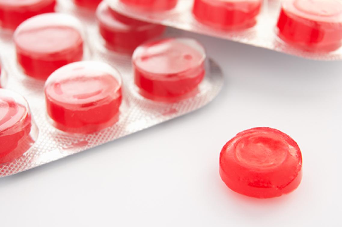 Packets of red coloured throat lozenges on a white background. Adobe