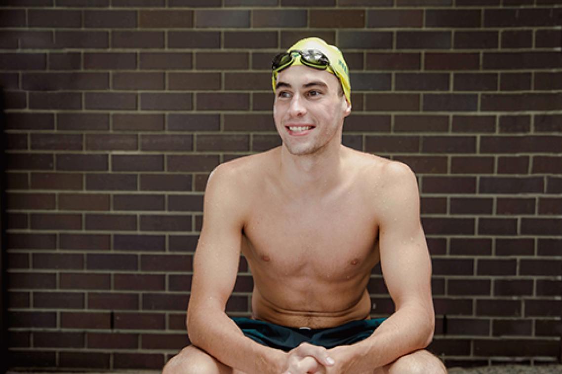 Thomas Neilll sitting with arms on his knees wearing his swimming cap and goggles