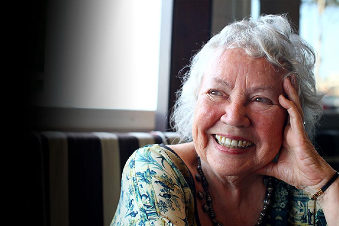 a grey-haired woman smiles resting her head on her hand