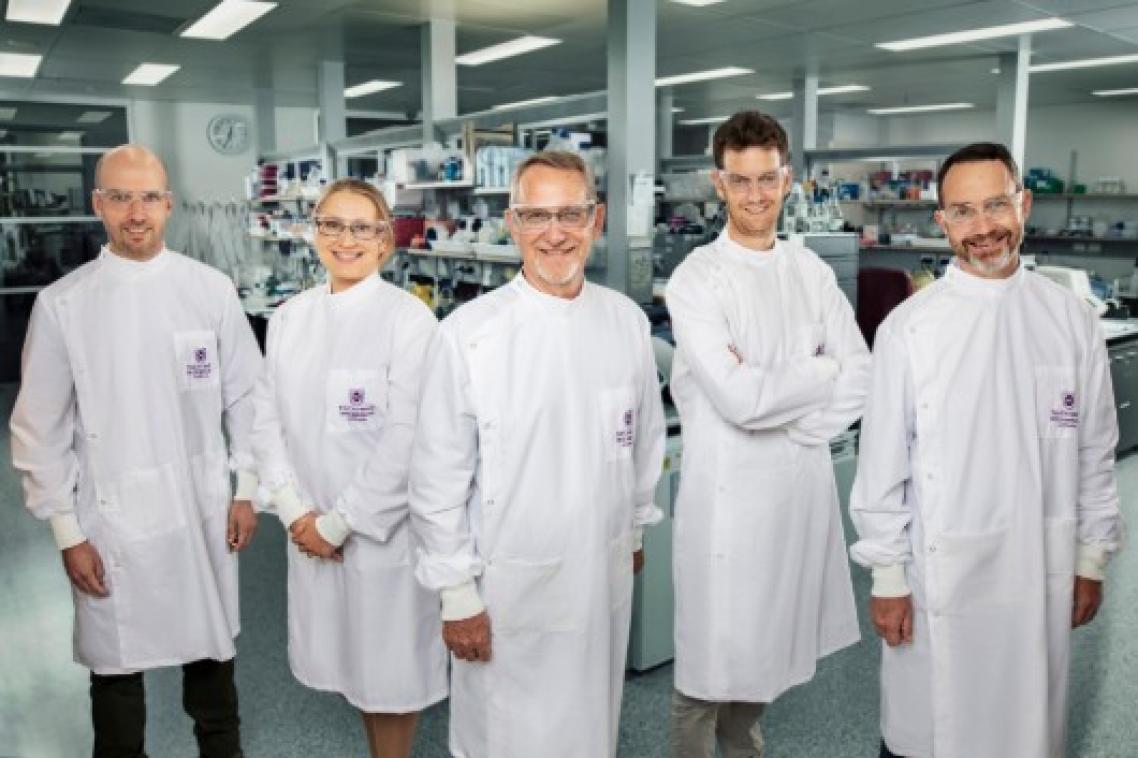 Five scientists in white lab coats stand in a row.